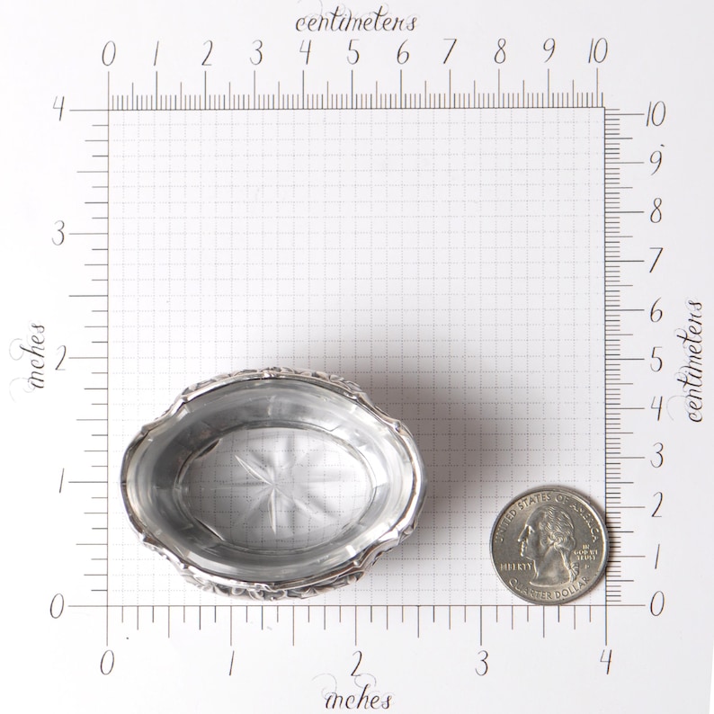 Puede incluir: Un peque&ntilde;o plato ovalado de plata con un borde decorativo. El plato mide aproximadamente 7,6 cm de largo y 5,1 cm de ancho. Una moneda est&aacute; al lado del plato para comparar el tama&ntilde;o. El plato tiene un dise&ntilde;o de estrella en el centro.