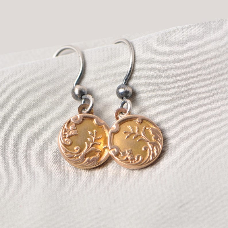 May include: A pair of gold-toned earrings with a floral design. The earrings are made of metal and have a silver hook.