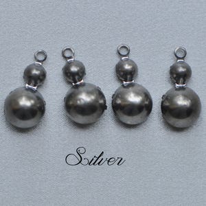 以下が含まれることがあります： ダブルボールのデザインのシルバー調の金属製チャームが4つ。各チャームの上部には、ネックレスやブレスレットに取り付けるための小さなループが付いています。
