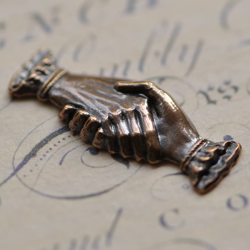 May include: A bronze sculpture of two hands clasped together in a handshake. The sculpture is detailed and realistic, with visible wrinkles and lines on the hands.