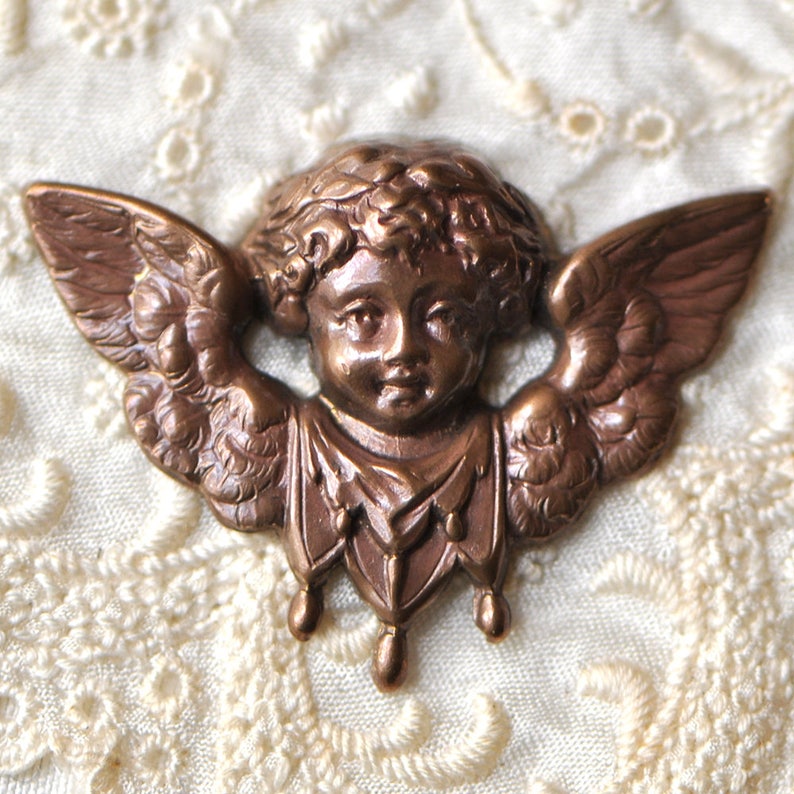 May include: A bronze cherub figurine with wings and a crown of leaves. The cherub has a delicate face and is wearing a flowing robe.