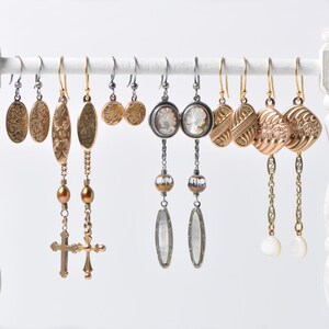 May include: A collection of eight pairs of dangle earrings with various styles and colors. The earrings feature gold, silver, and clear glass beads, as well as cross and floral designs.