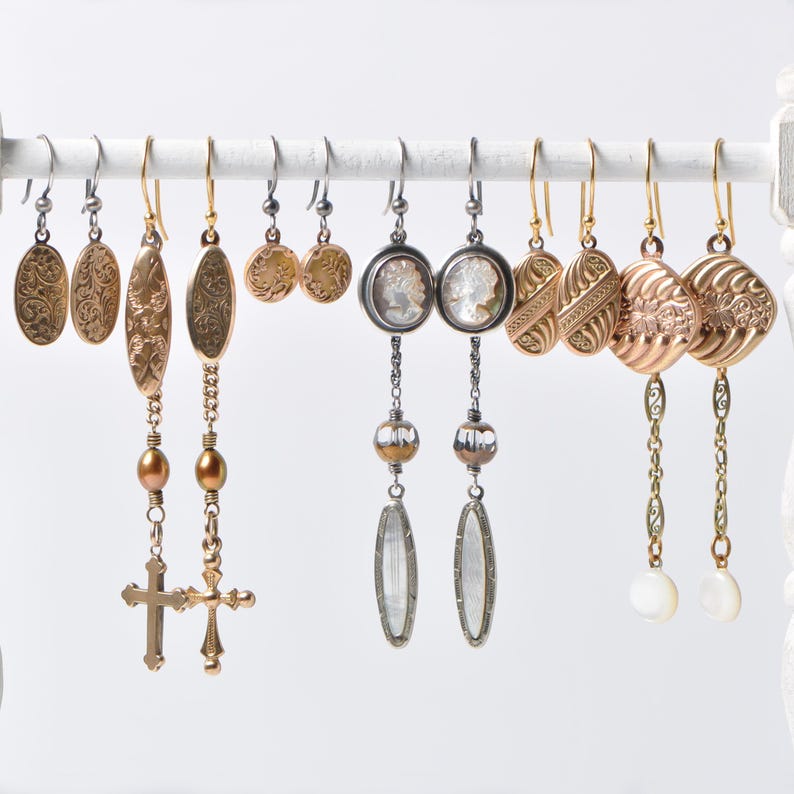 May include: A collection of eight pairs of dangle earrings with various styles and colors. The earrings feature gold, silver, and clear glass beads, as well as cross and floral designs.