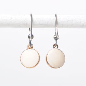 May include: A pair of white ceramic disc earrings with gold trim and silver hooks.