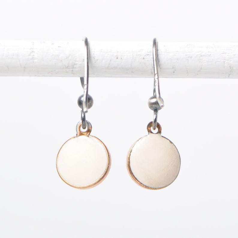 May include: A pair of white ceramic disc earrings with gold trim and silver hooks.