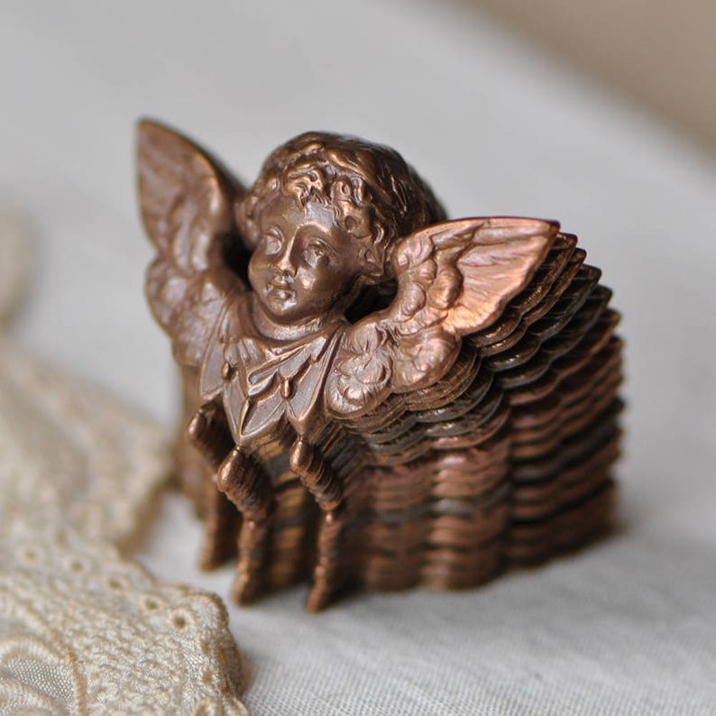 May include: A stack of vintage copper angel charms with a detailed design. Each charm features a cherub with wings and a delicate face.