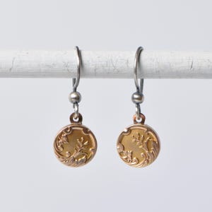May include: A pair of gold earrings with a floral design. The earrings are made of silver and have a delicate, vintage look.