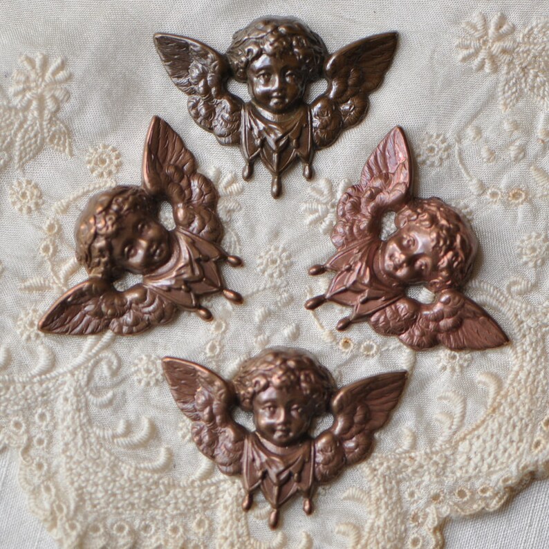 May include: Four antique-style metal angel figurines with wings, each with a different pose and expression. The angels are made of a copper-toned metal and have a distressed finish.