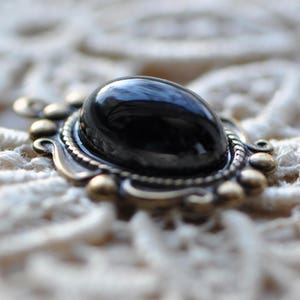May include: A black gemstone pendant with an ornate silver setting. The pendant is on a white lace background.