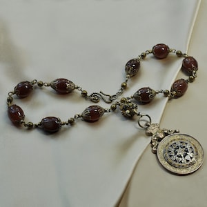 Può includere: Una collana di perle di cornalina marrone con un ciondolo dorato con un design a stella dettagliato.