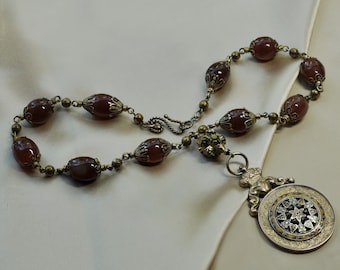 May include: A brown carnelian bead necklace with a gold-toned pendant featuring a detailed starburst design.