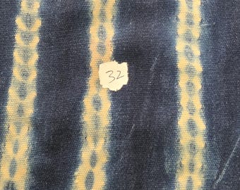 Könnte beinhalten: Ein dunkelblauer Stoff mit drei vertikalen Streifen in einem hellgelben Kettenmuster. Ein kleines weißes Papieretikett mit der handschriftlichen Nummer 32 ist in der Mitte des Stoffes befestigt, der eine deutlich sichtbare Webstruktur aufweist.