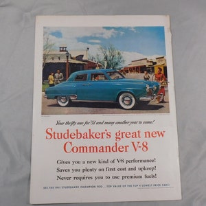 Könnte beinhalten: Eine Vintage-Werbung für den Studebaker Commander V-8. Die Anzeige zeigt ein blaues Auto, das vor einer Westernstadt geparkt ist. Der Text lautet: "Ihr sparsames Auto für 1951 und viele weitere Jahre! Der neue Studebaker Commander V-8 bietet Ihnen eine neue Art von V-8-Leistung! Spart Ihnen viel bei den Anschaffungskosten und der Wartung! Benötigt nie Premium-Kraftstoff!"