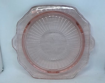 Puede incluir: Un plato para pastel de vidrio rosa con un borde festoneado y un diseño de sol en el centro.
