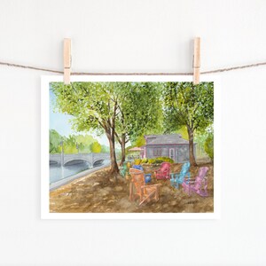 May include: Watercolour painting of a small grey building with a red roof and a bridge in the background. There are colourful chairs in front of the building, and green trees on either side.