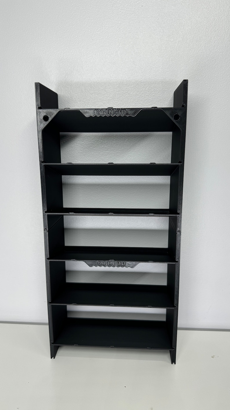 May include: Black plastic shelf unit with six shelves. The shelves are evenly spaced and have a slight lip on the front edge. The unit is freestanding and has a simple, modern design.