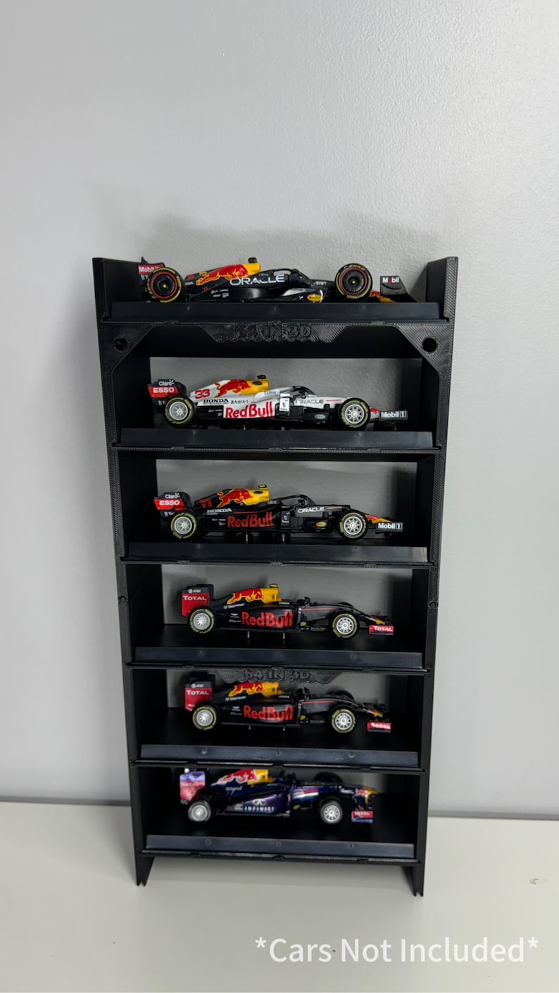 May include: Black wall shelf with six levels for displaying miniature Formula 1 race cars. The shelf is made of 3D printed plastic and has a textured surface. The text "Cars Not Included" is printed on the bottom of the shelf.