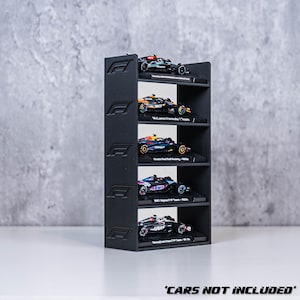 May include: A black display shelf with five levels, each holding a miniature Formula 1 race car. The shelf has the Formula 1 logo on the sides. The text "CARS NOT INCLUDED" is at the bottom.