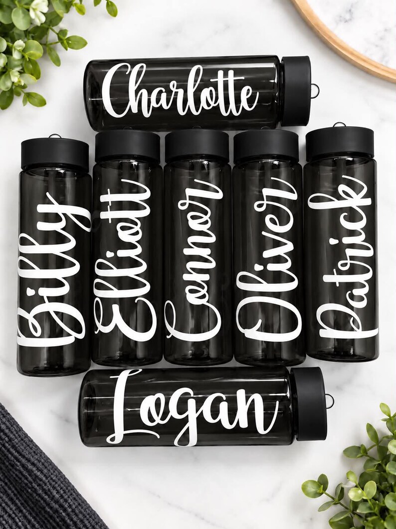 Pu&ograve; includere: Una collezione di sette borracce nere trasparenti con tappi a vite neri. Ogni borraccia presenta un nome bianco stampato in un carattere corsivo. I nomi visualizzati sono Charlotte, Billy, Elliott, Connor, Oliver, Patrick e Logan.