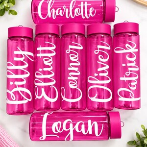 May include: Seven translucent hot pink plastic water bottles with matching screw-top lids. Each bottle features a unique white script name printed on the side, including the names Charlotte, Billy, Elliott, Connor, Oliver, Patrick, and Logan.