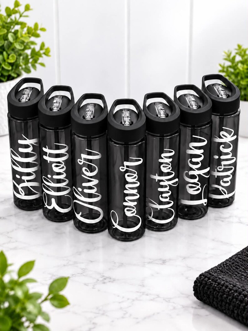 Pu&ograve; includere: Sette borracce in plastica nera traslucida disposte a semicerchio. Ogni borraccia presenta un tappo nero con una cannuccia trasparente a scatto ed &egrave; personalizzata con un nome in corsivo bianco: Billy, Elliott, Oliver, Connor, Clayton, Logan e Patrick.