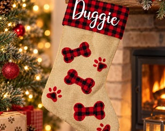 May include: A tan burlap Christmas stocking featuring a red and black buffalo plaid cuff with the name Duggie written in white script. The stocking is decorated with three red and black buffalo plaid dog bone appliques and paw prints.