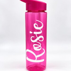May include: A translucent hot pink water bottle with a matching lid and a flip-top spout. The name Rosie is printed vertically on the side of the bottle in large, white, cursive script lettering. The bottle is cylindrical and made of plastic.