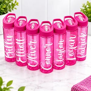 May include: Seven translucent hot pink plastic water bottles arranged in a semi-circle. Each bottle features a matching pink lid with a carry handle and a white script name printed vertically: Billy, Elliott, Oliver, Connor, Clayton, Logan, and Patrick.