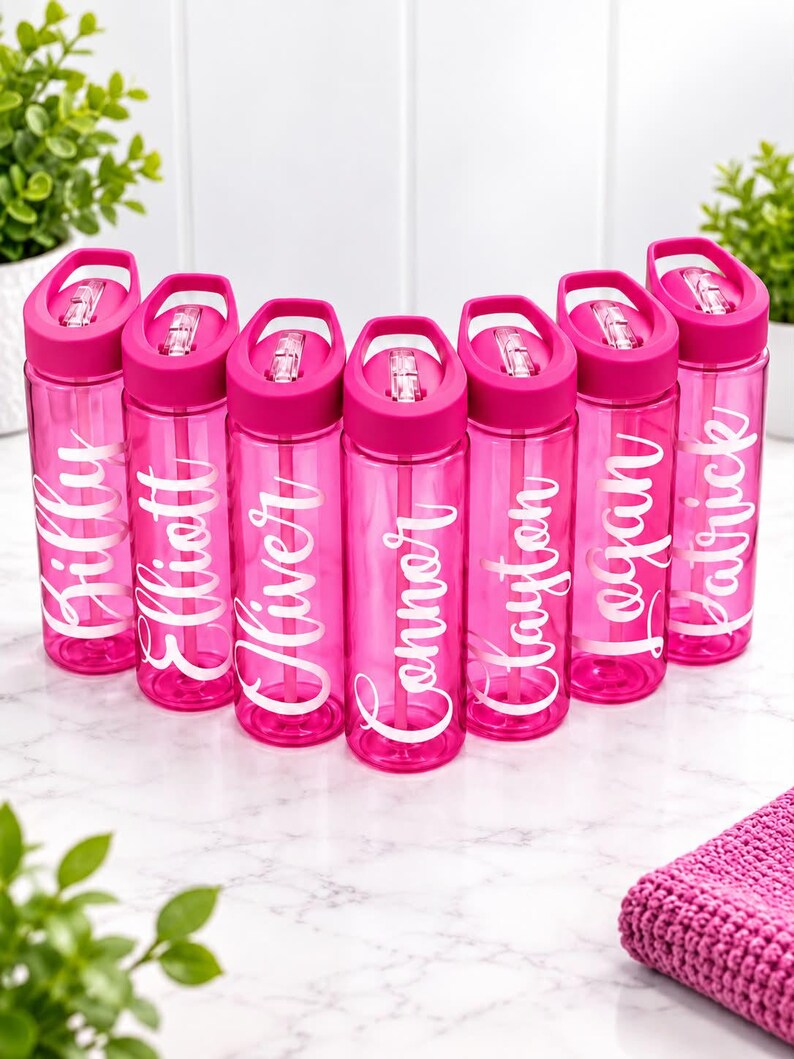 May include: Seven translucent hot pink plastic water bottles arranged in a semi-circle. Each bottle features a matching pink lid with a carry handle and a white script name printed vertically: Billy, Elliott, Oliver, Connor, Clayton, Logan, and Patrick.