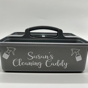 May include: Grey plastic cleaning caddy with a black handle and a white label that says "Susan's Cleaning Caddy".
