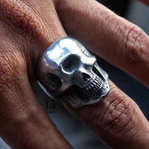 Puede incluir: Un anillo de calavera de plata con un diseño detallado. El anillo se lleva en un dedo.