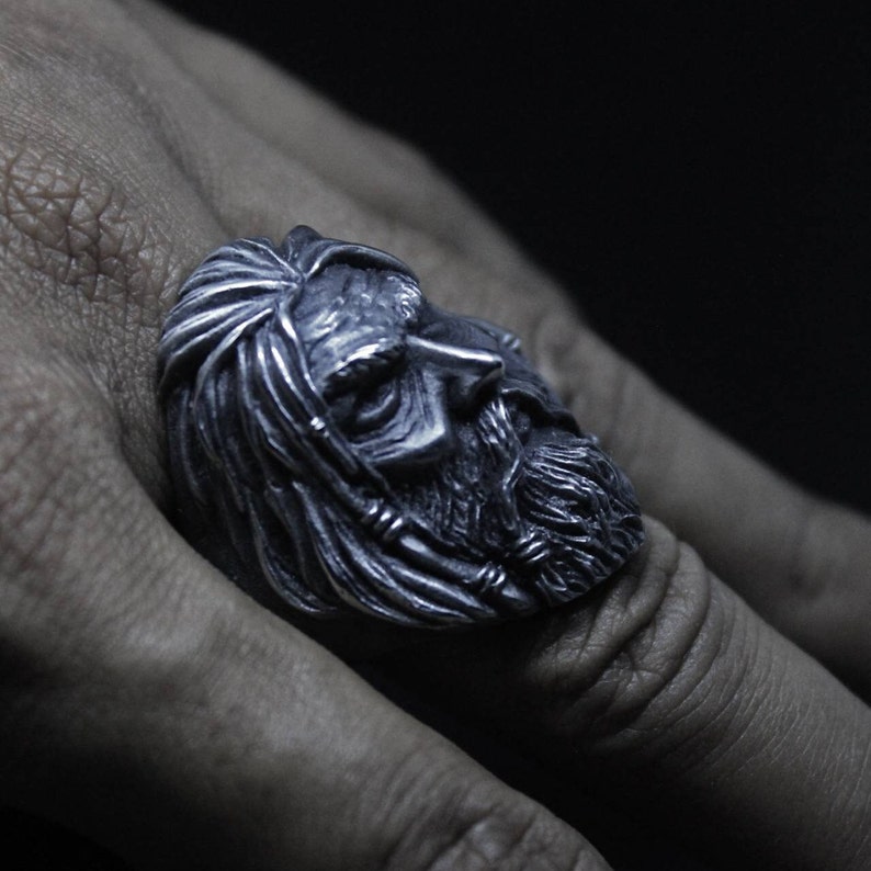 Puede incluir: Un anillo de plata con una escultura detallada de la cara de un hombre con una larga barba. El anillo se lleva en el dedo de una persona.