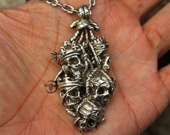 May include: A silver pendant necklace featuring a cluster of five skull charms, each with a crown and intricate details. The skulls are connected by a rope-like design.