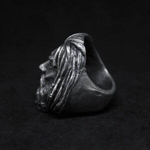 Puede incluir: Un anillo de plata con un rostro esculpido detallado de un hombre con cabello largo y barba. El anillo se muestra de lado.