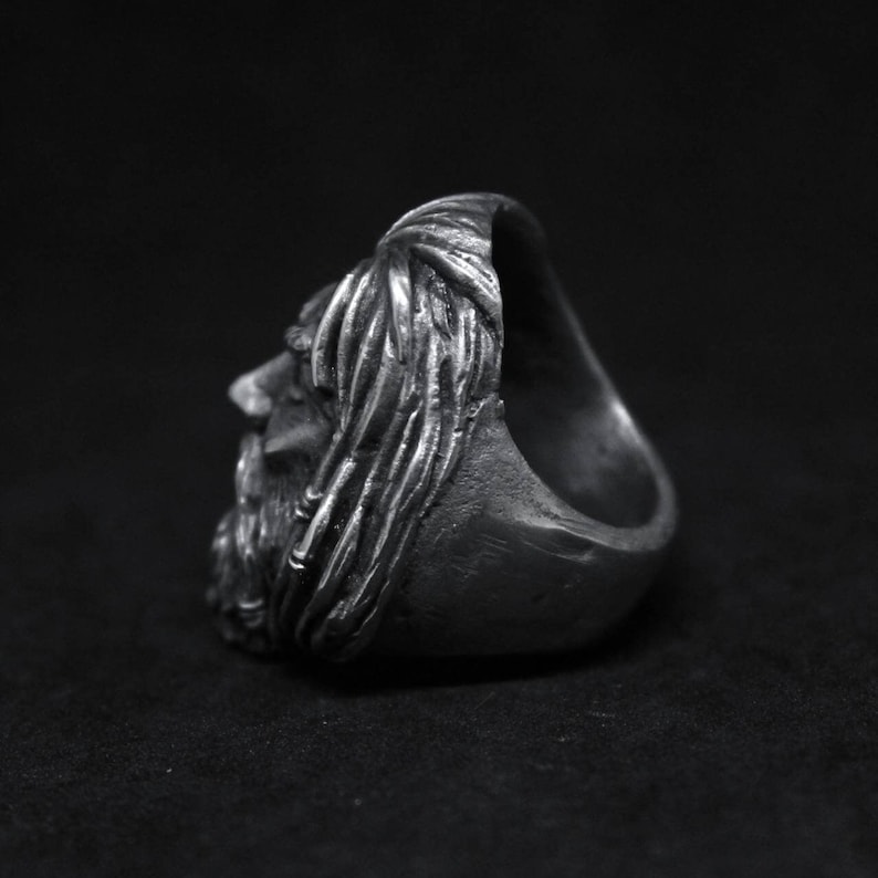 Puede incluir: Un anillo de plata con un rostro esculpido detallado de un hombre con cabello largo y barba. El anillo se muestra de lado.