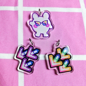 May include: Three clear acrylic charms with colorful designs. One charm features a white cartoon character with sunglasses. The other two charms feature a rainbow-colored arrow design.