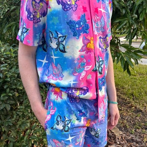 May include: A pink and blue button-up shirt and matching shorts with a whimsical print of cartoon fairies and stars.