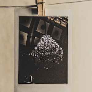 May include: A black and white photo of a large, ornate chandelier hanging from a ceiling with a grid pattern. The chandelier is made of many small, crystal-like pieces.