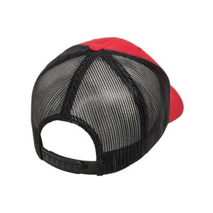 Puede incluir: Una gorra de camionero roja y negra con la parte trasera de malla. La gorra tiene una correa ajustable negra.