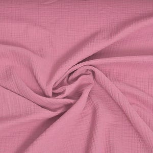 May include: A close-up shot of a soft, pink fabric with a textured, crinkled appearance. The fabric is draped and folded, creating shadows and highlights that emphasize its texture. The color is a muted, dusty rose.