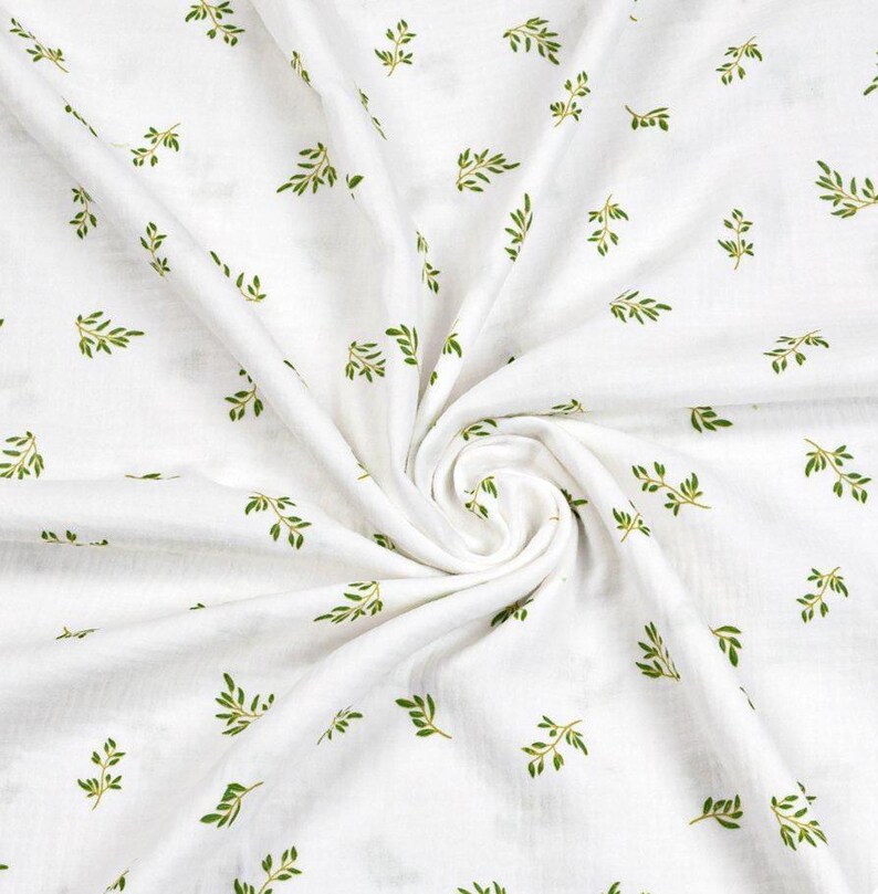 May include: White fabric with a repeating pattern of small green leaves. The leaves are detailed with visible veins and are scattered across the fabric. The fabric is gathered in a swirl, creating shadows and texture.