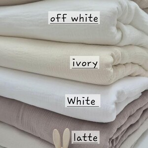 May include: A stack of folded fabric in various neutral colors, including sand, off-white, ivory, white, latte, and linen. A wooden bunny figurine and cotton sprig are in the foreground. The fabric is labeled with its color name.