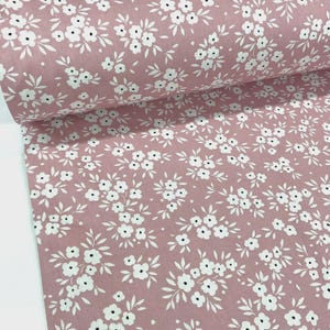 Puede incluir: Un rollo de tela con un estampado floral repetitivo. La tela tiene un fondo rosa empolvado con flores y hojas blancas. Las flores son peque&ntilde;as y agrupadas, creando un dise&ntilde;o delicado y femenino. Ideal para proyectos de costura.