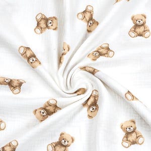 May include: White fabric with a repeating pattern of brown teddy bears. The bears are in various poses, some upright and others lying down. The fabric has a soft, textured appearance.
