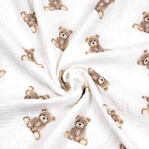 May include: White fabric with a repeating pattern of brown teddy bears in various poses. The bears have detailed features and are scattered across the soft, textured material. The fabric appears to be lightweight and suitable for baby items.