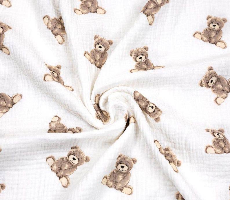 May include: White fabric with a repeating pattern of brown teddy bears in various poses. The bears have detailed features and are scattered across the soft, textured material. The fabric appears to be lightweight and suitable for baby items.