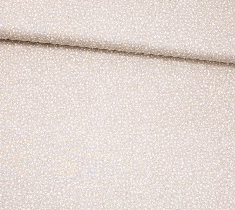 Puede incluir: Tela beige con un sutil patr&oacute;n de peque&ntilde;os puntos blancos irregulares. La tela est&aacute; doblada, mostrando una ligera textura y variaci&oacute;n de color. La apariencia general es suave y neutra, adecuada para varios proyectos de costura.