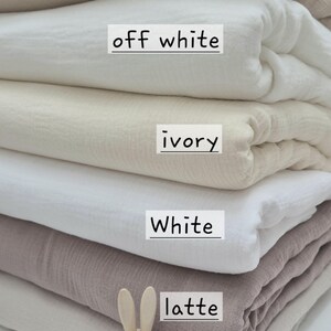 May include: A stack of folded fabric in various neutral colors, including sand, off-white, ivory, white, latte, and linen. Each fabric color is labeled with its name. A small wooden bunny figurine is placed near the bottom of the stack.