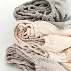 Peut inclure: Une pile de trois draps-housses de couleurs neutres. Le drap supérieur est gris, le drap du milieu est beige et le drap inférieur est beige clair. Chaque drap a un bord élastique. Les draps sont en tissu texturé.