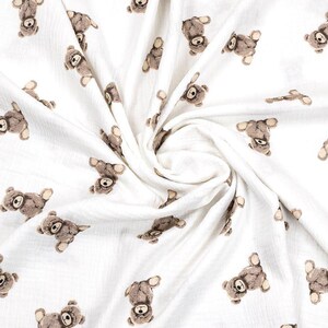 May include: White fabric with a repeating pattern of brown teddy bears. The bears are in various poses, with their heads and limbs visible. The fabric is soft and appears to be a lightweight material, suitable for baby blankets or clothing.